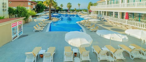 A pool area with sun loungers, umbrellas, and a building with a balcony.