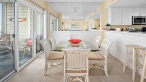 A dining area with a glass table and wicker chairs, a kitchen with white cabinets, and a sliding glass door leading to an outdoor area.