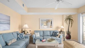 A living room with two sofas, a coffee table, a ceiling fan, and a large window with a view.