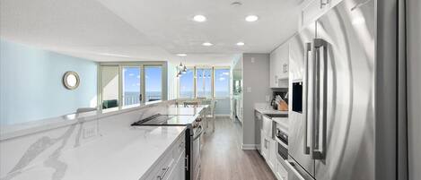 A modern kitchen with a large island, stainless steel appliances, and a view to the outside.