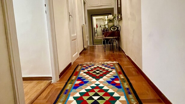 Un couloir avec un tapis à motifs, un plancher en bois, des murs blancs et un luminaire suspendu.