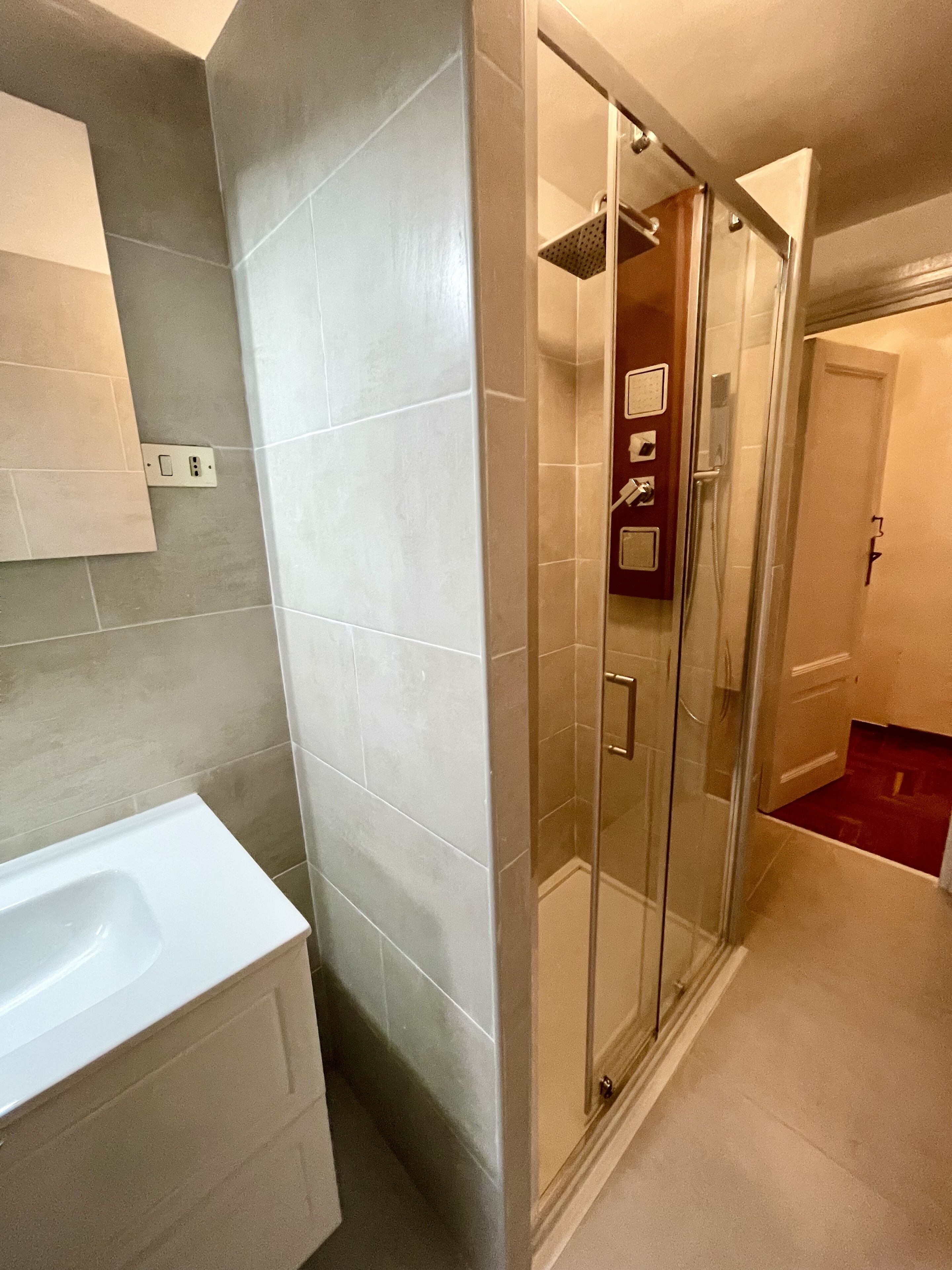 A modern bathroom with a glass shower enclosure, a white sink, and a tiled floor.