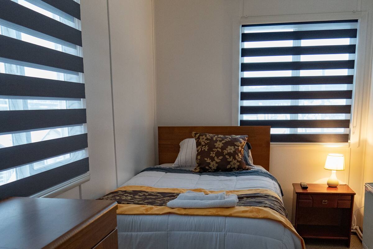 Ein Hotelzimmer mit einem Bett, einem Holzschrank, einem Nachttisch mit Lampe und einem Fenster mit Jalousien.
