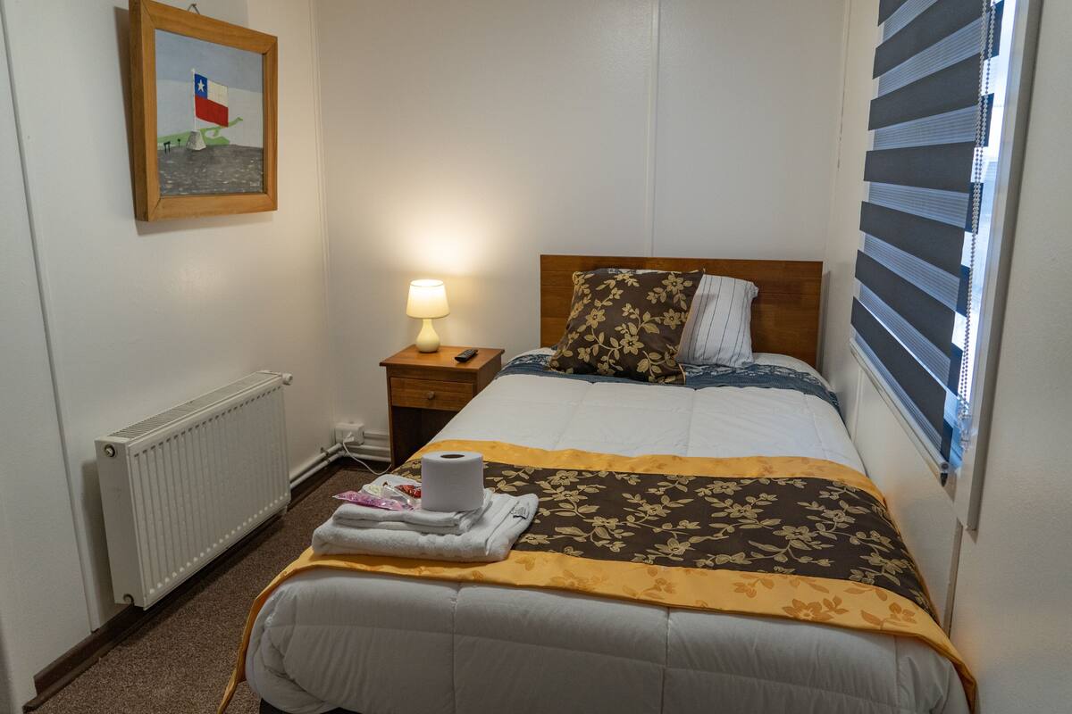 Ein Hotelzimmer mit Bett, Nachttisch mit Lampe, Heizkörper und einem gerahmten Bild an der Wand.