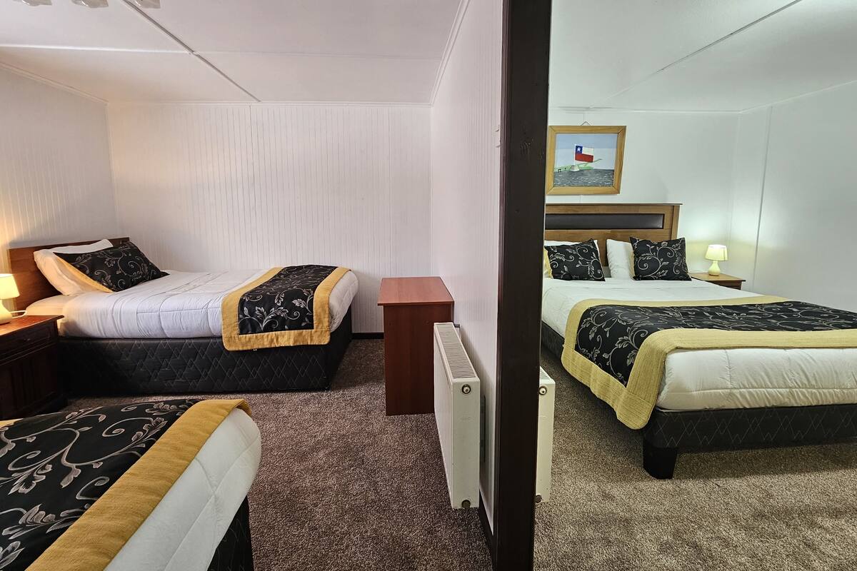 Ein Hotelzimmer mit zwei Betten, einem Holfnachtkästchen, einem Heizkörper und einem gerahmten Bild an der Wand.