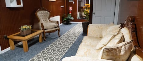 Una habitación con alfombra estampada, un sofá, una silla y una mesita con una planta.