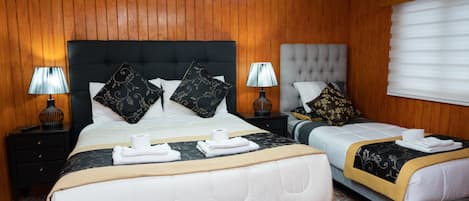 Habitación de hotel con dos camas, paneles de madera y un amplio ventanal con persianas.