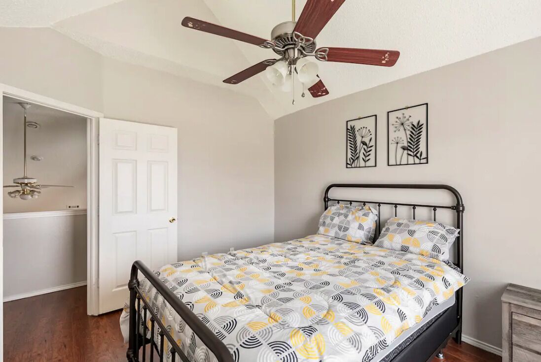 A bedroom with a bed, a ceiling fan, a door, and wall art.