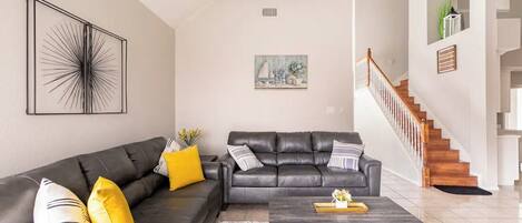 A living room with a black leather sofa, a coffee table, and a staircase.