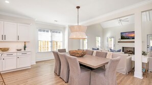 A modern kitchen with white cabinetry, a dining table with cushioned chairs, and a fireplace. - Private Heated Pool & Spa | Close to Beaches, Restaurants & Shopping! (Saint Simons Island)