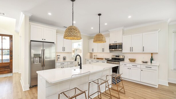 A modern kitchen with white cabinetry, a stainless steel refrigerator, a large island with bar stools, and two hanging pendant lights. - Private Heated Pool & Spa | Close to Beaches, Restaurants & Shopping! (Saint Simons Island)