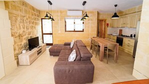 Una sala de estar moderna con una pared de piedra, un televisor, un juego de sofá y una zona de comedor con una mesa y sillas.