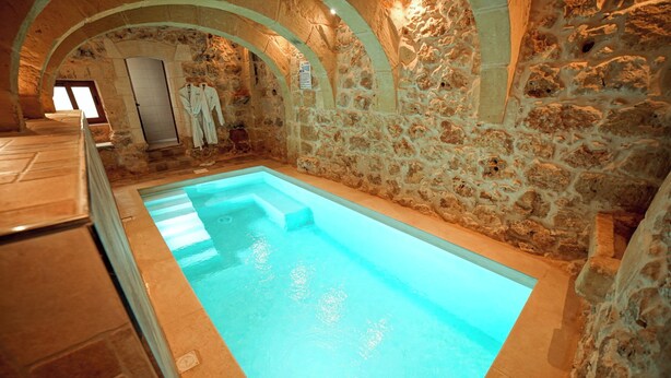Une piscine intérieure aux murs en pierre et aux plafonds en forme d’arc.