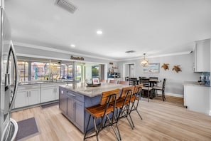 A modern kitchen with a central island, bar stools, and a dining area with a view of the outdoors.
