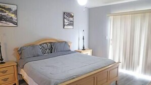 A bedroom with a bed, a nightstand, a lamp, a window with curtains, and two wall-mounted paintings. - Spacious Condo Near Disney (Kissimmee)