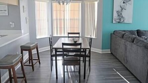 A dining area with a table and chairs, a sofa, and a painting on the wall. - Spacious Condo Near Disney (Kissimmee)