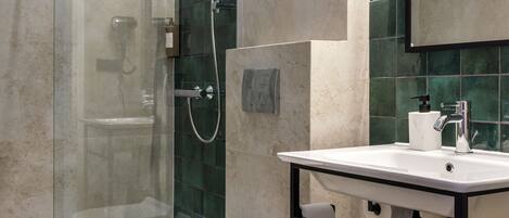 Un baño moderno con ducha envuelta en vidrio, inodoro blanco y lavamanos con estructura de metal negro.