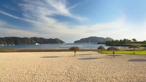 Una playa con cielo despejado, orilla de arena y vista al mar con barcos.