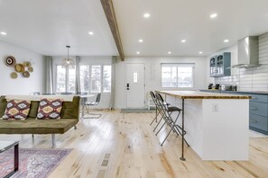 Una cocina moderna con una isla central, un comedor con sofá y sillones, y un ventanal que aporta luz natural.