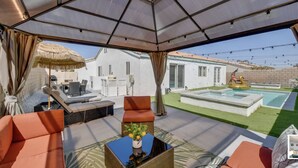 An outdoor patio with seating, a pool, and a covered area with a view of a house and garden. - Indio Oasis with pool, jacuzzi, gazebo , grill, fire pit and a game room (Indio)