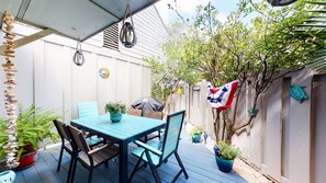 Eine überdachte Terrasse mit Tisch und Stühlen, umgeben von Kübelpflanzen und einem dekorativen Zaun.