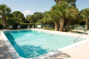 Ein rechteckiger Swimmingpool mit klarem, blauem Wasser, umgeben von Palmen und einem Zaun.