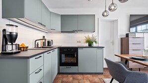 A modern kitchen with grey cabinets, a built-in oven, a coffee maker, and a dining area with a table and chair.