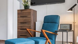 A modern living room with a blue upholstered chair, a wooden cabinet, a flat-screen TV, a Marshall speaker, and a table with a candle.