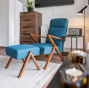Un salon moderne avec un fauteuil bleu recouvert de tissu, un meuble en bois, un téléviseur à écran plat, un haut-parleur Marshall et une table avec une bougie.