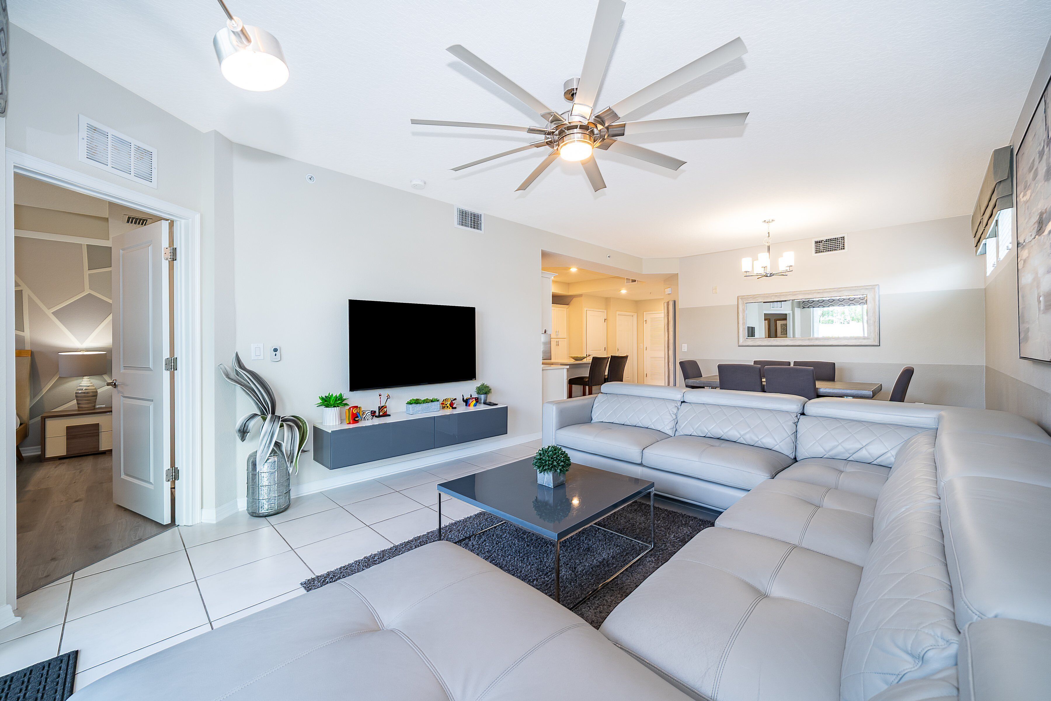 A modern living room with a sectional sofa, a flat-screen TV, and a ceiling fan.