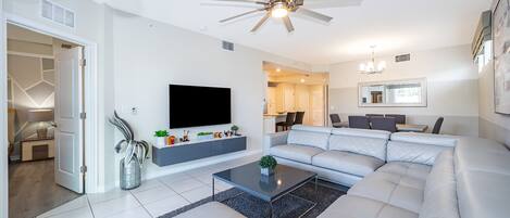 A modern living room with a sectional sofa, a flat-screen TV, and a ceiling fan.