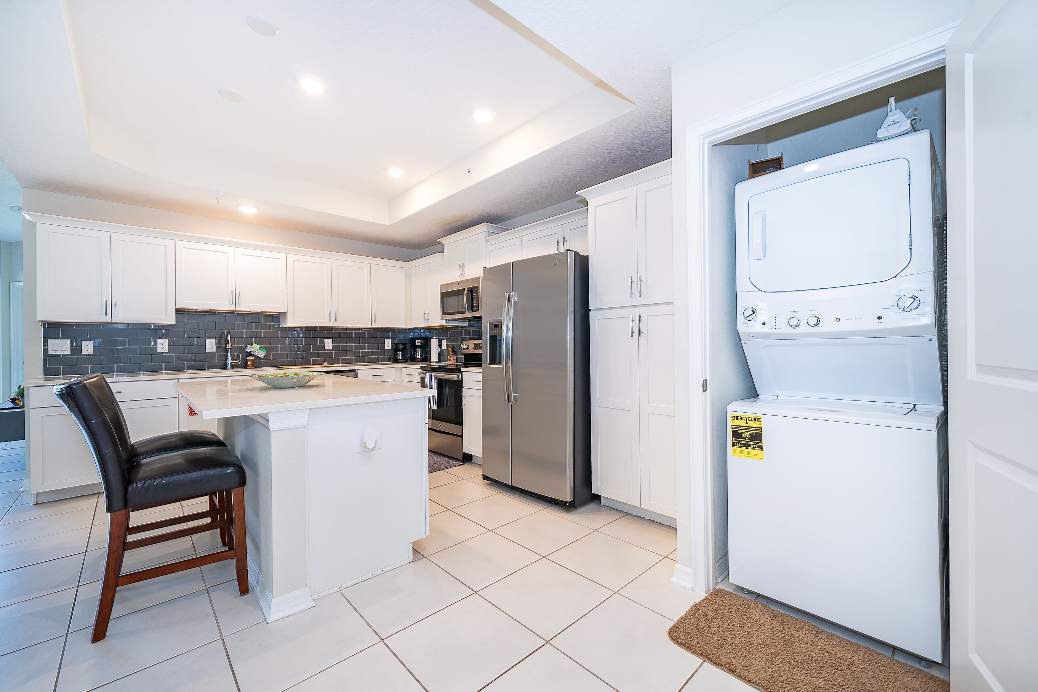 A modern kitchen with white cabinetry, stainless steel appliances, and a central island with seating.