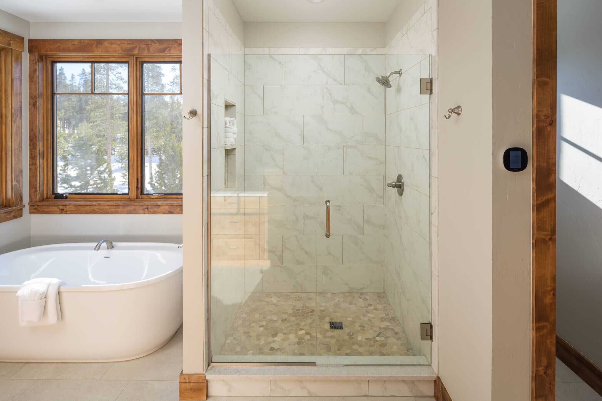 Ein modernes Badezimmer mit einer freistehenden Badewanne, einer Duschkabine und einem Fenster mit Blick auf Bäume.