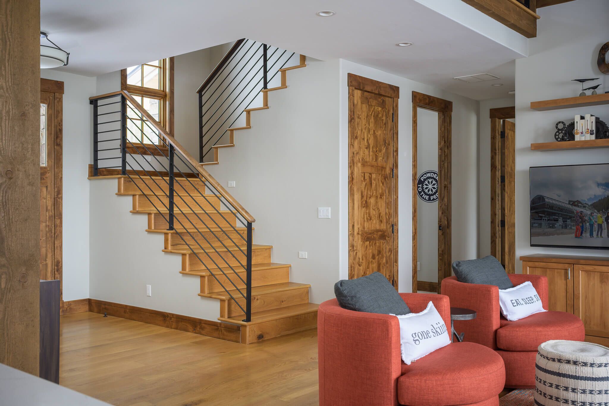 Ein modernes Wohnzimmer mit einer Holztreppe, roten Sofas und einem großen Fernseher.