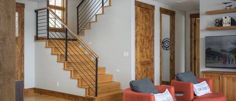 Ein modernes Wohnzimmer mit einer Holztreppe, roten Sofas und einem großen Fernseher.