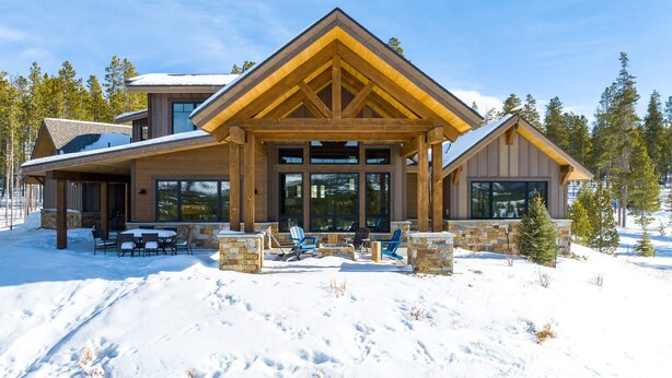 Un chalet moderne avec des fondations en pierre, de grandes fenêtres et un patio couvert.