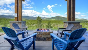 Un espace extérieur aménagé, abrité et doté d’un foyer en pierre et de fauteuils Adirondack, offrant une vue sur un paysage montagneux.