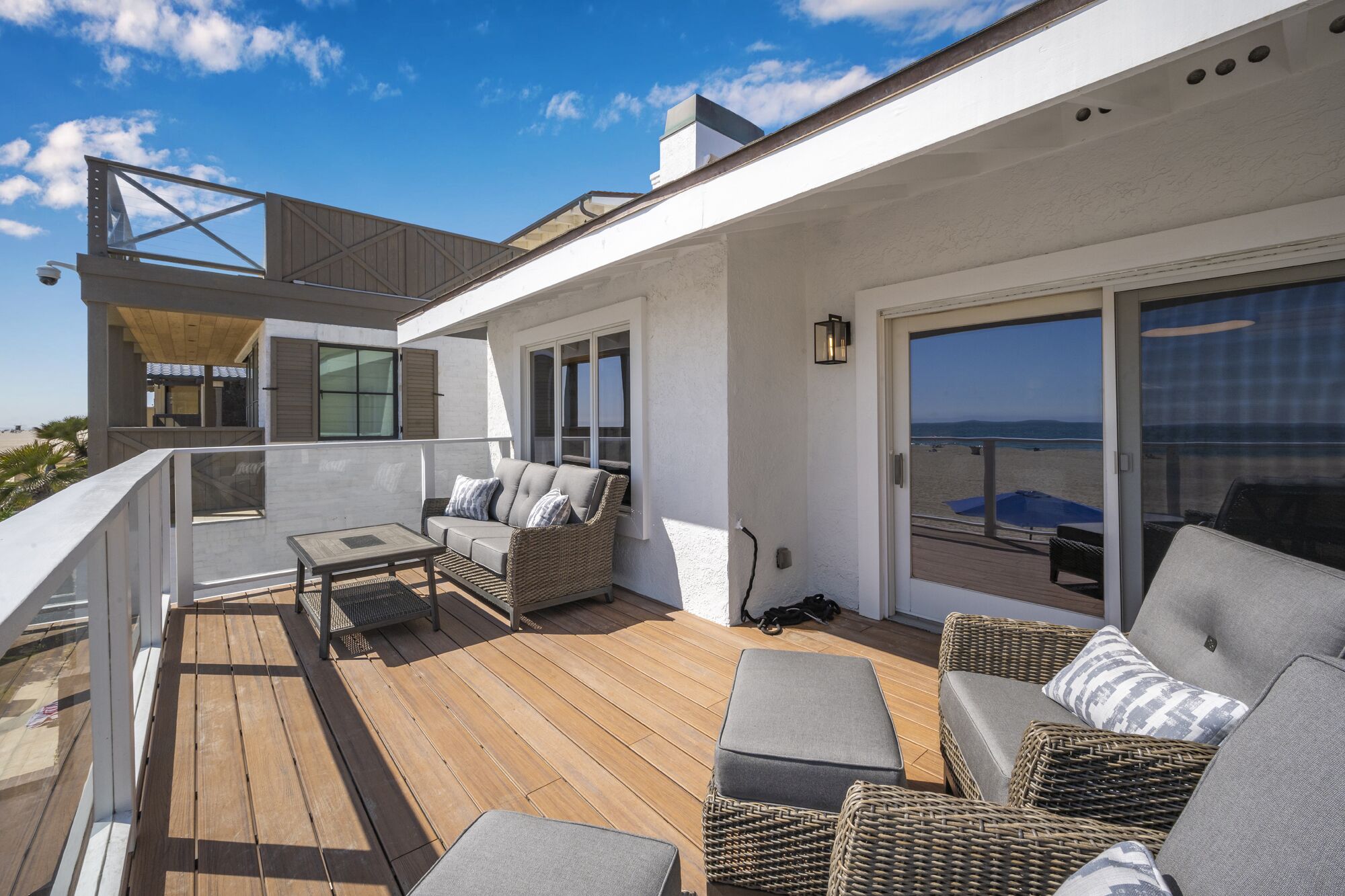Een modern terras buiten met rieten meubels, een houten tafel en uitzicht op de oceaan.
