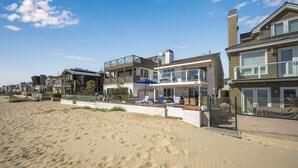 Une propriété située en bord de mer, comprenant des maisons à plusieurs étages, une plage de sable et un espace piscine avec des chaises longues.