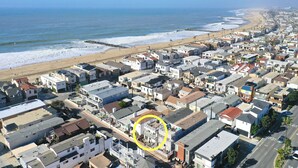 Luftaufnahme einer Küstenwohngegend mit Strand, Häusern und einem markierten Gebäude.