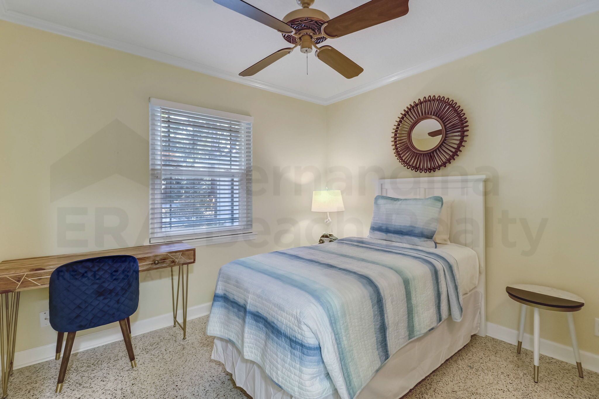 A bedroom with a bed, a desk, a chair, a ceiling fan, a window with blinds, and a wall mirror.