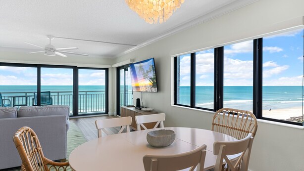 A spacious living area with a large window overlooking the ocean, a ceiling fan, and a dining table with chairs. - ✨ Updated Direct Oceanfront Corner 2/2 | Large Wrap-Around Balcony 🌅 | Heated Pool (New Smyrna Beach)