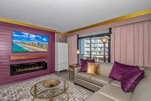A living room with a TV, fireplace, sofa, and a view of a building through a window.