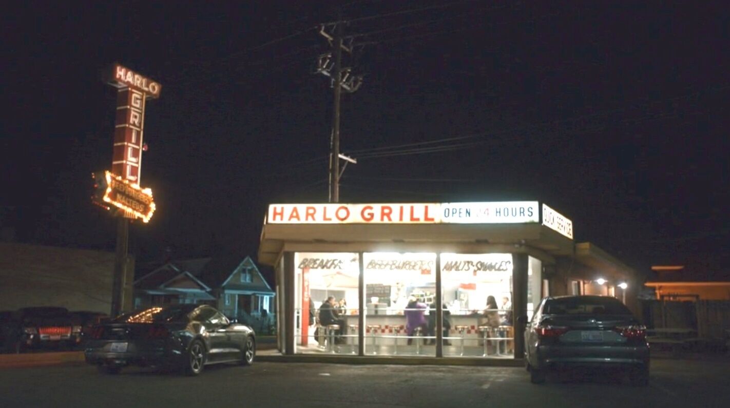 Vista nocturna de un restaurante llamado 'Harlo Grill' con un letrero que indica que está abierto las 24 horas.