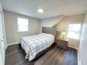 A bedroom with a bed, a nightstand, a lamp, and two windows.