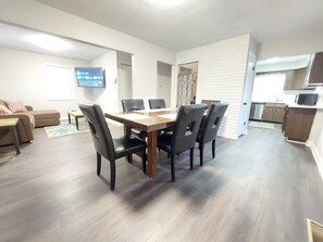 A modern living room with a dining table, chairs, a sofa, and a TV.