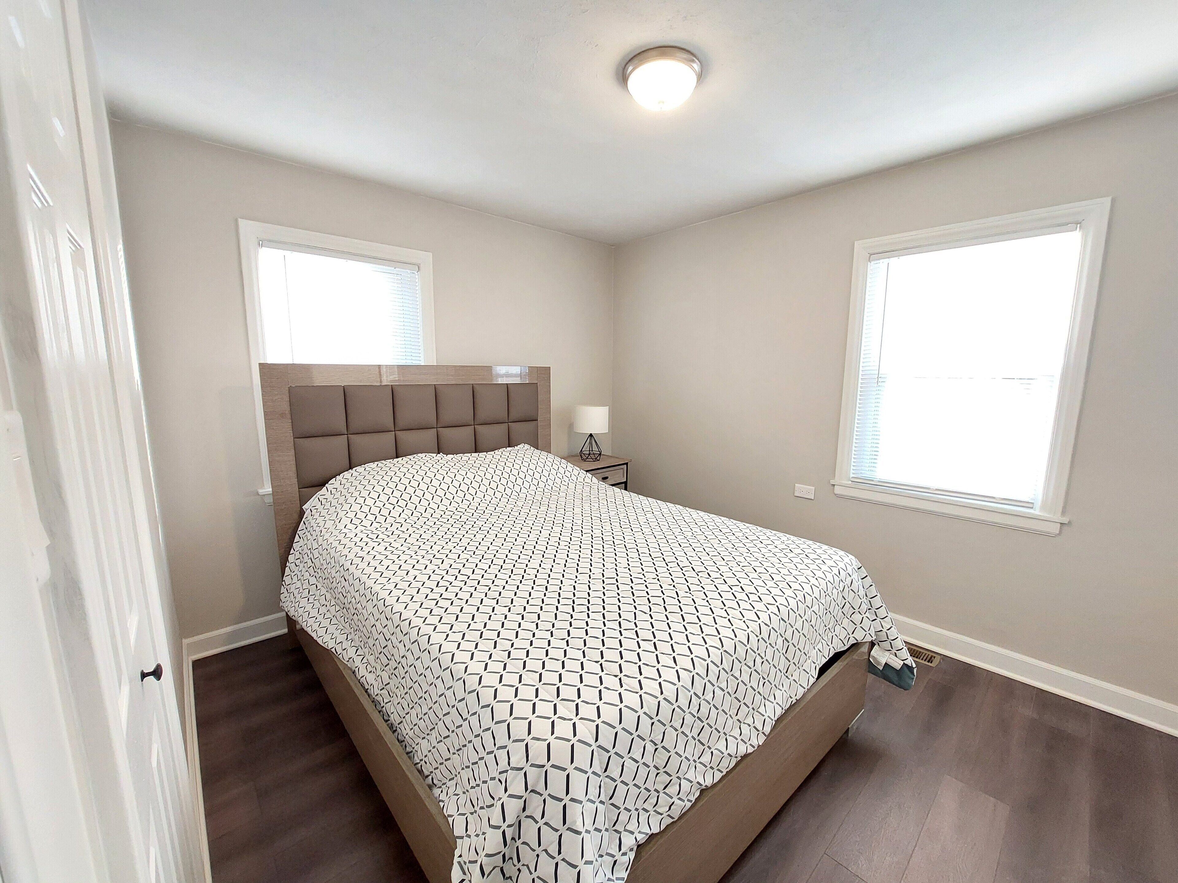A bedroom with a bed, a nightstand, a window, and a ceiling light.