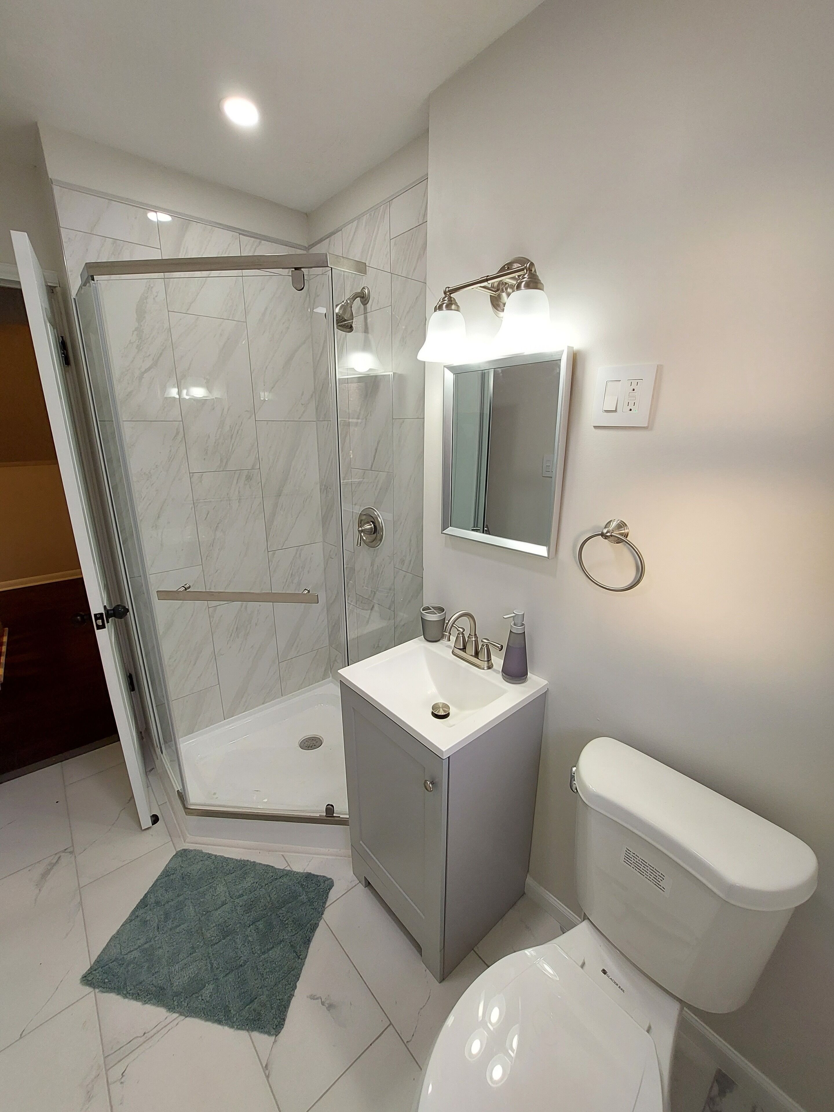 A modern bathroom with a glass shower enclosure, a white sink with a mirror above, and a toilet.