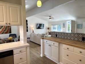 A modern kitchen with white cabinetry, a wooden countertop, and a dining area with a glass table and patterned chairs. - A MidMod Sanctuary (Palm Springs)