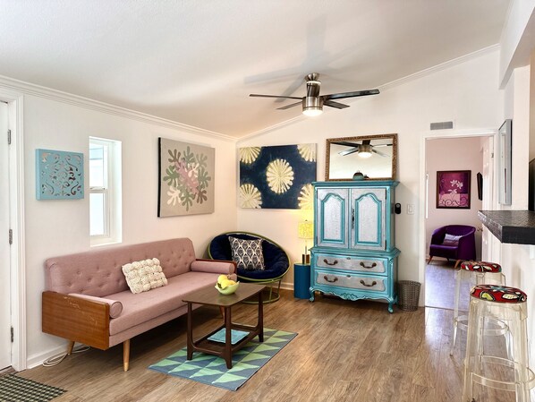 A living room with a pink sofa, a blue armchair, a wooden coffee table, a teal cabinet, and a ceiling fan. - A MidMod Sanctuary (Palm Springs)